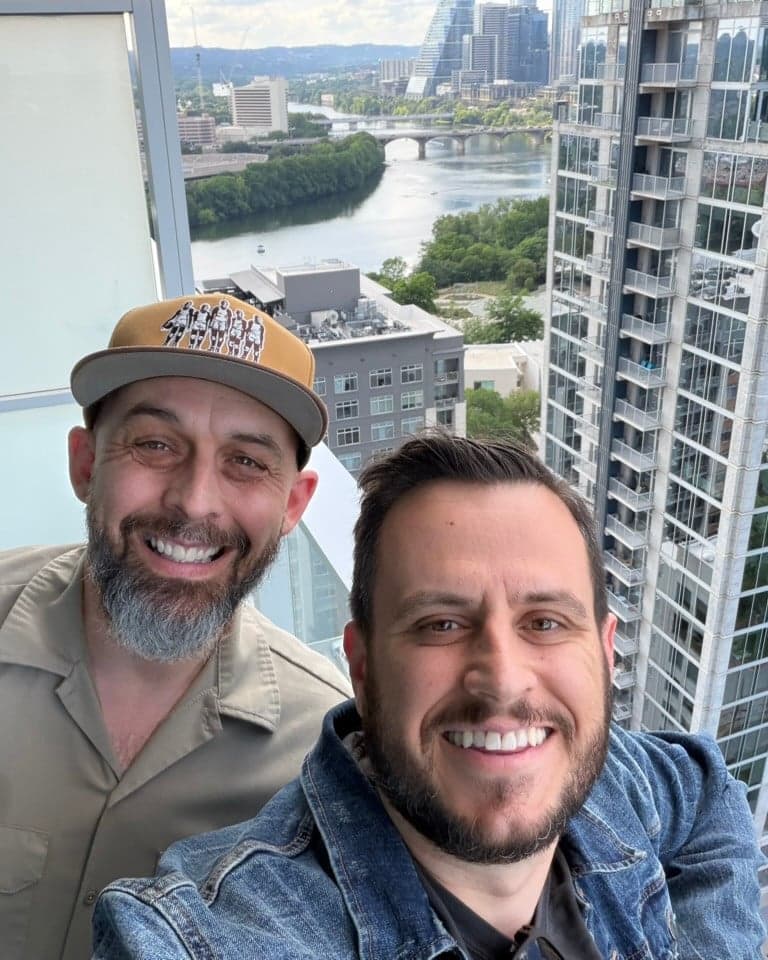 Aaron Edwards and Josh Dailey smiling on a balcony overlooking the river and Austin skyline